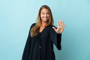 Mavi arka planda izole edilmiş orta yaşlı Brezilyalı kadın parmaklarıyla beşi sayıyor.