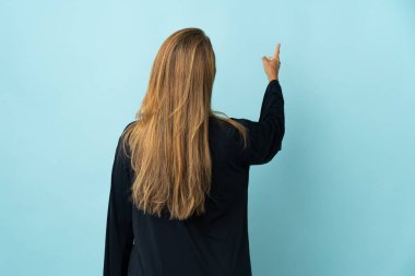 Mavi arka planda izole edilmiş orta yaşlı Brezilyalı kadın işaret parmağıyla işaret ediyor.