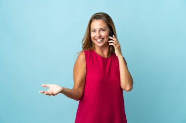 Mavi arka planda izole edilmiş orta yaşlı Brezilyalı bir kadın cep telefonuyla sohbet ediyor.