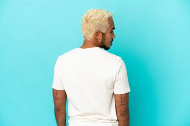 Genç Kolombiyalı yakışıklı adam mavi arka planda izole edilmiş.