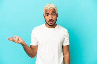 Genç Kolombiyalı yakışıklı adam mavi arka planda izole edilmiş şüpheli hareketler yapıyor.
