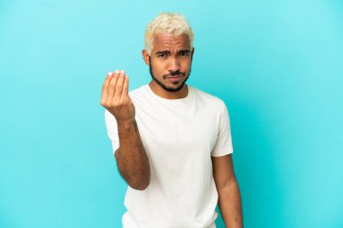Mavi arka planda izole edilmiş genç Kolombiyalı yakışıklı adam İtalyan jestleri yapıyor.