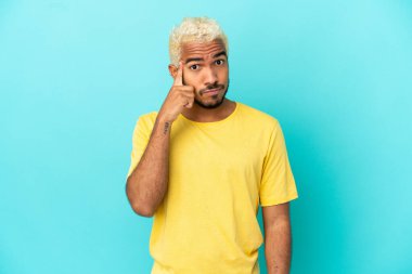 Genç Kolombiyalı yakışıklı adam mavi arka planda izole edilmiş bir fikir düşünüyor.