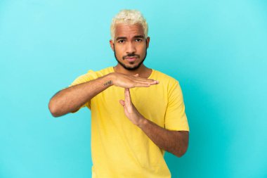 Genç Kolombiyalı yakışıklı adam mavi arka planda izole edilmiş.