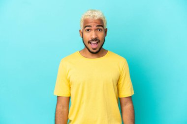 Genç Kolombiyalı yakışıklı adam mavi arka planda izole edilmiş ve yüzünde sürpriz bir ifade var.