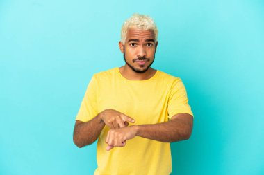 Genç Kolombiyalı yakışıklı adam mavi arka planda izole edilmiş, geç kalma jesti yapıyor.