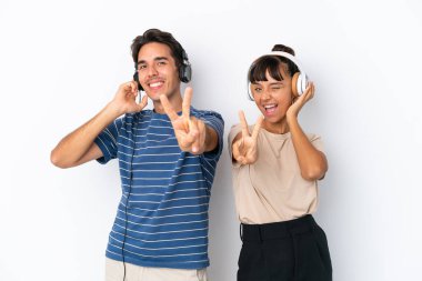 Beyaz arka planda izole edilmiş genç melez arkadaşlar müzik dinliyor ve şarkı söylüyorlar.