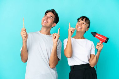 Mavi arka planda saç kurutma makinesi ve diş fırçası tutan genç bir çift işaret parmağıyla işaret etmek harika bir fikir.