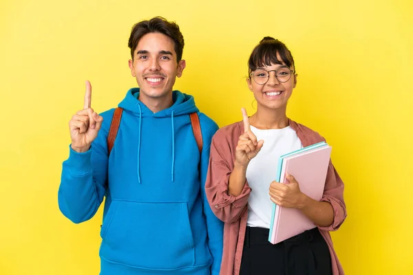 一对年轻的学生夫妇在黄色的背景上彼此隔离 伸出一个手指 表示他们是最好的一对 — 图库照片