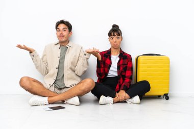 Genç melez ırk yolcuları, beyaz arka planda izole bir şekilde oturuyorlar. El ve omuzlarını kaldırırken şüpheleri var.