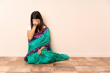 Genç Hintli kadın baş ağrısıyla yerde oturuyor.