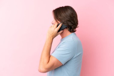 Üst düzey Hollandalı, pembe arka planda izole edilmiş bir şekilde cep telefonuyla sohbet ediyor.