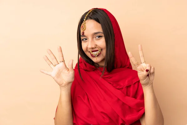 在米色背景上被隔离的年轻印度女人用手指数到七 — 图库照片