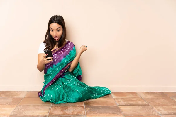 坐在地板上的年轻印度女人吃惊地发出了一个信息 — 图库照片