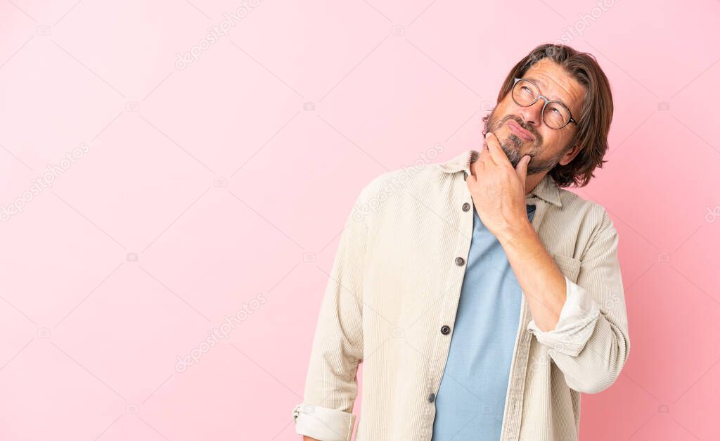 Senior dutch man isolated on pink background having doubts