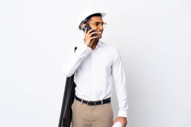 Miğferli Afrikalı Amerikalı mimar ve izole edilmiş beyaz arka plan üzerinde planları var. Cep telefonuyla sohbet ediyor.