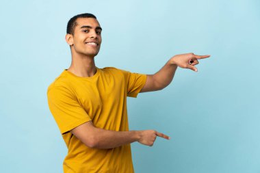 İzole edilmiş arka planda yaşayan Afro-Amerikalı bir adam parmağını yana uzatıp bir ürün sunuyor.