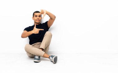 Afro-Amerikalı bir adam yerde oturmuş yüzüne odaklanıyor. Çerçeve sembolü