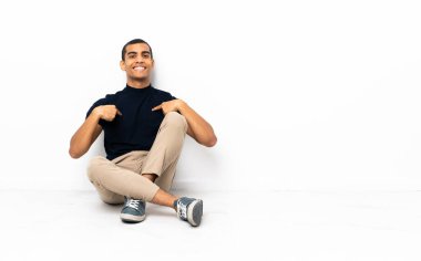 Afro-Amerikalı bir adam yerde oturuyor ve yüzünde sürpriz bir ifade var.