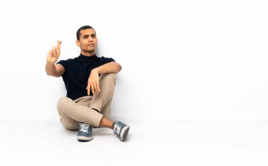 Afro-Amerikan bir adam yerde oturuyor ve en iyisini diliyor.