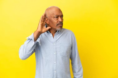 Küba Senior 'u sarı arka planda izole edilmiş. Kulağına elini koyarak bir şeyler dinliyor.
