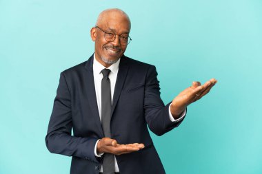 İşletme son sınıf öğrencisi mavi arka planda izole edilmiş ve davet edilmek için ellerini yana uzatıyor.