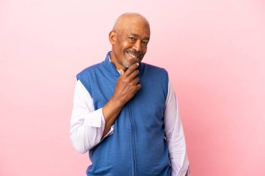 Kübalı son sınıf öğrencisi pembe arka planda izole edilmiş, yana bakıyor ve gülümsüyor.