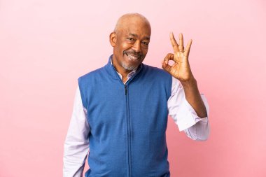 Kübalı son sınıf öğrencisi pembe arka planda izole edildi. Parmaklarıyla tamam işareti gösteriyor.