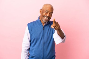 Kübalı son sınıf öğrencisi pembe arka planda izole edilmiş, şaşırmış ve ön tarafı işaret ediyor