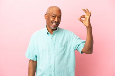 Kübalı son sınıf öğrencisi pembe arka planda izole edildi. Parmaklarıyla tamam işareti gösteriyor.