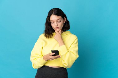 Genç Ukraynalı kız mavi arka planda izole edilmiş düşünüyor ve bir mesaj gönderiyor.