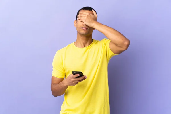 Afroamerykanin Nad Odizolowanym Fioletowym Tle Pomocą Telefonu Komórkowego Zakrywa Oczy — Zdjęcie stockowe