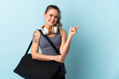 Spor çantalı genç Brezilyalı kadın mavi arka planda izole edilmiş bir ürün sunmak için yan tarafı işaret ediyor.