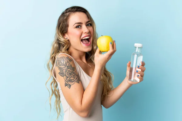 用苹果和一瓶水隔离在蓝色背景下的巴西年轻女子 — 图库照片
