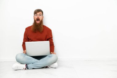 Dizüstü bilgisayarı olan genç, beyaz arka planda yüzü şaşırmış beyaz bir adam.