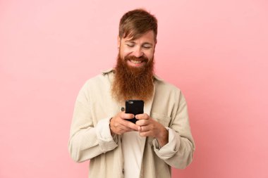 Pembe arka planda izole edilmiş genç beyaz adam cep telefonuyla bir mesaj gönderiyor.