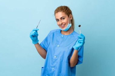 Genç kadın diş hekimi mavi arka planda aletler tutuyor.
