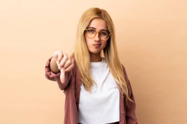Genç Uruguaylı sarışın kadın, izole edilmiş arka planda, olumsuz bir ifadeyle baş parmağını gösteriyor.