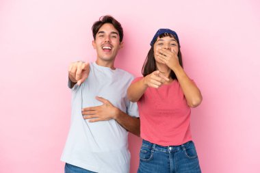 Pembe arka planda izole edilmiş genç bir çift birini işaret ediyor ve çok gülüyor.