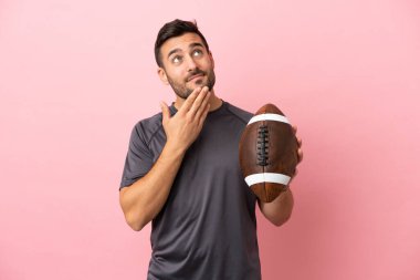 Genç beyaz adam pembe arka planda izole edilmiş rugby oynuyor gülümserken yukarı bakıyor