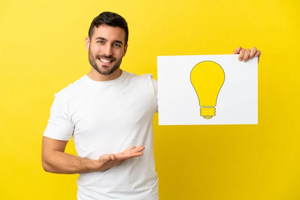 Young Handsome Caucasian Man Isolated Yellow Background Holding Placard Bulb — Stock Photo, Image