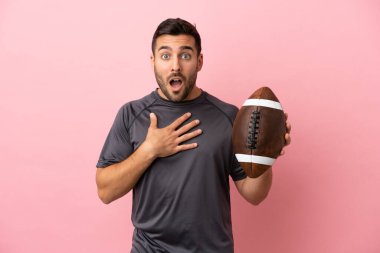 Pembe arka planda ragbi oynayan genç beyaz adam şaşırdı ve şaşırdı.