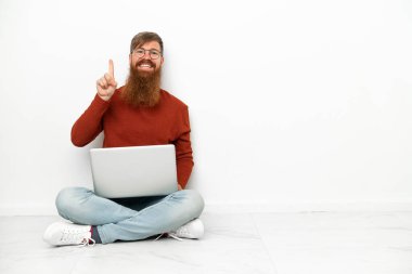 Dizüstü bilgisayarlı genç beyaz adam beyaz arka planda izole edilmiş ve en iyinin işareti olarak parmağını kaldırıyor.