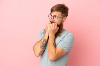 Pembe arka planda izole edilmiş, genç, kızıl, beyaz bir adam gergin ve elleri ağıza vermeye korkuyor.