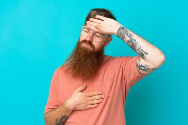 Kırmızımsı beyaz adam mavi arka planda gözlüklü ve yorgun.