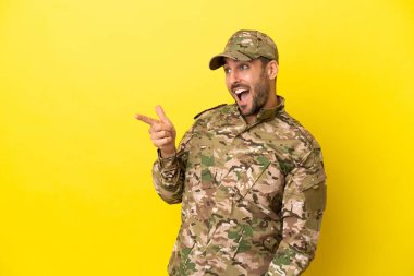 Asker, sarı arka planda izole edilmiş bir şekilde parmak ucunda bir ürün sunuyor.