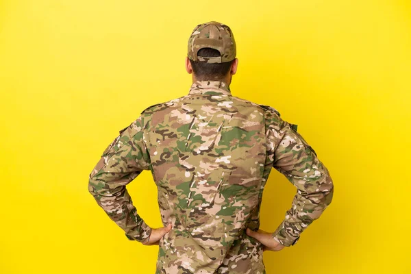 Military man isolated on yellow background in back position
