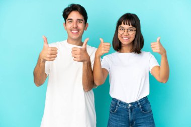 Mavi arka planda soyutlanmış melez bir çift iki eliyle baş parmak işareti yapıyor ve gülümsüyor.