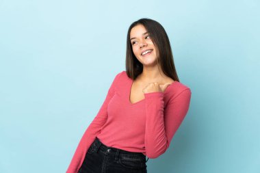 Mavi arka planda izole edilmiş genç bir kız bir ürünü sunmak için kenarı işaret ediyor.