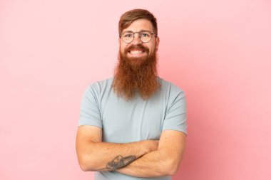 Pembe arka planda izole edilmiş genç beyaz adam kollarını ön cephede çapraz tutuyor.